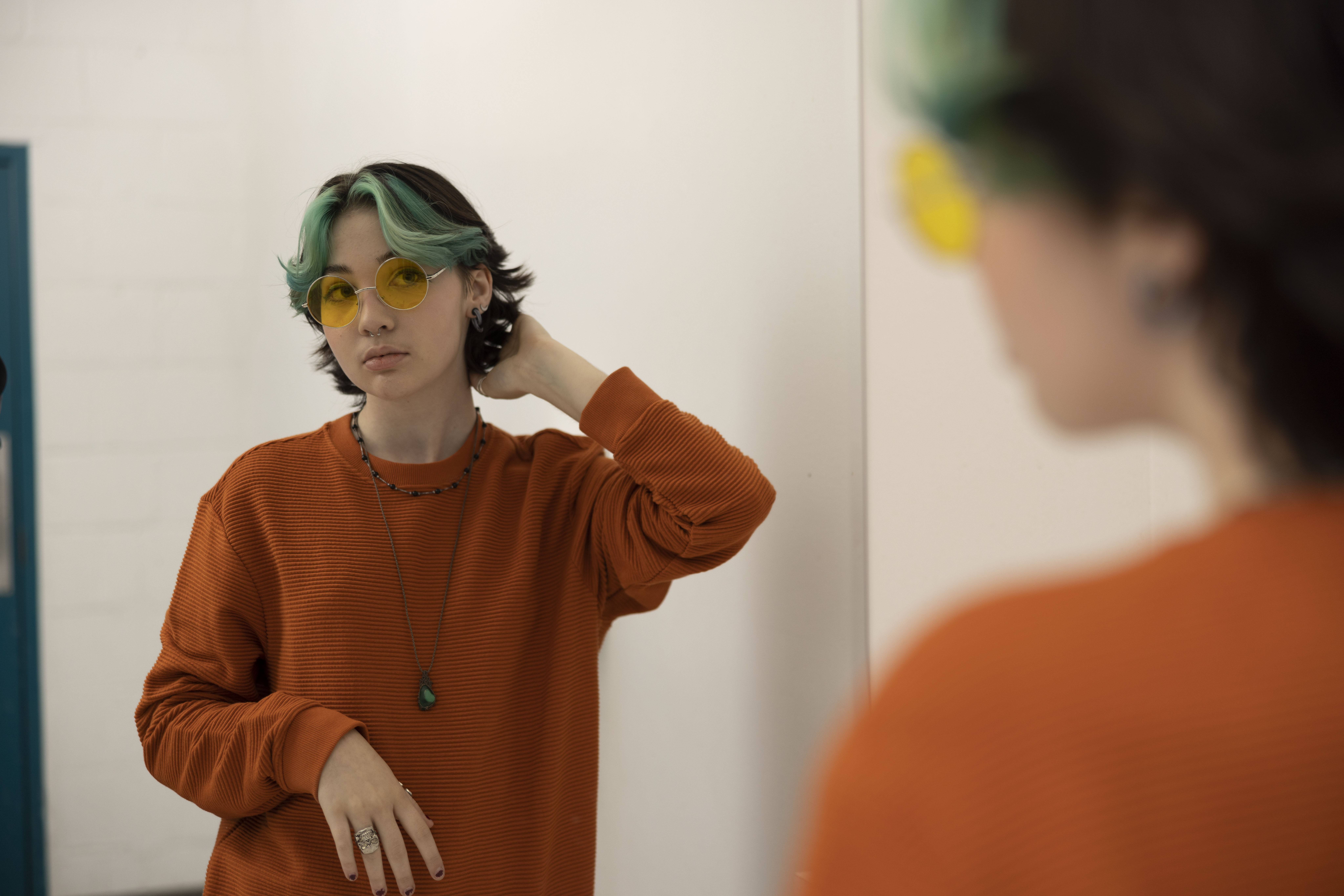 Young person wearing an orange sweatshirt looking at themselves in the mirror thinking about body image